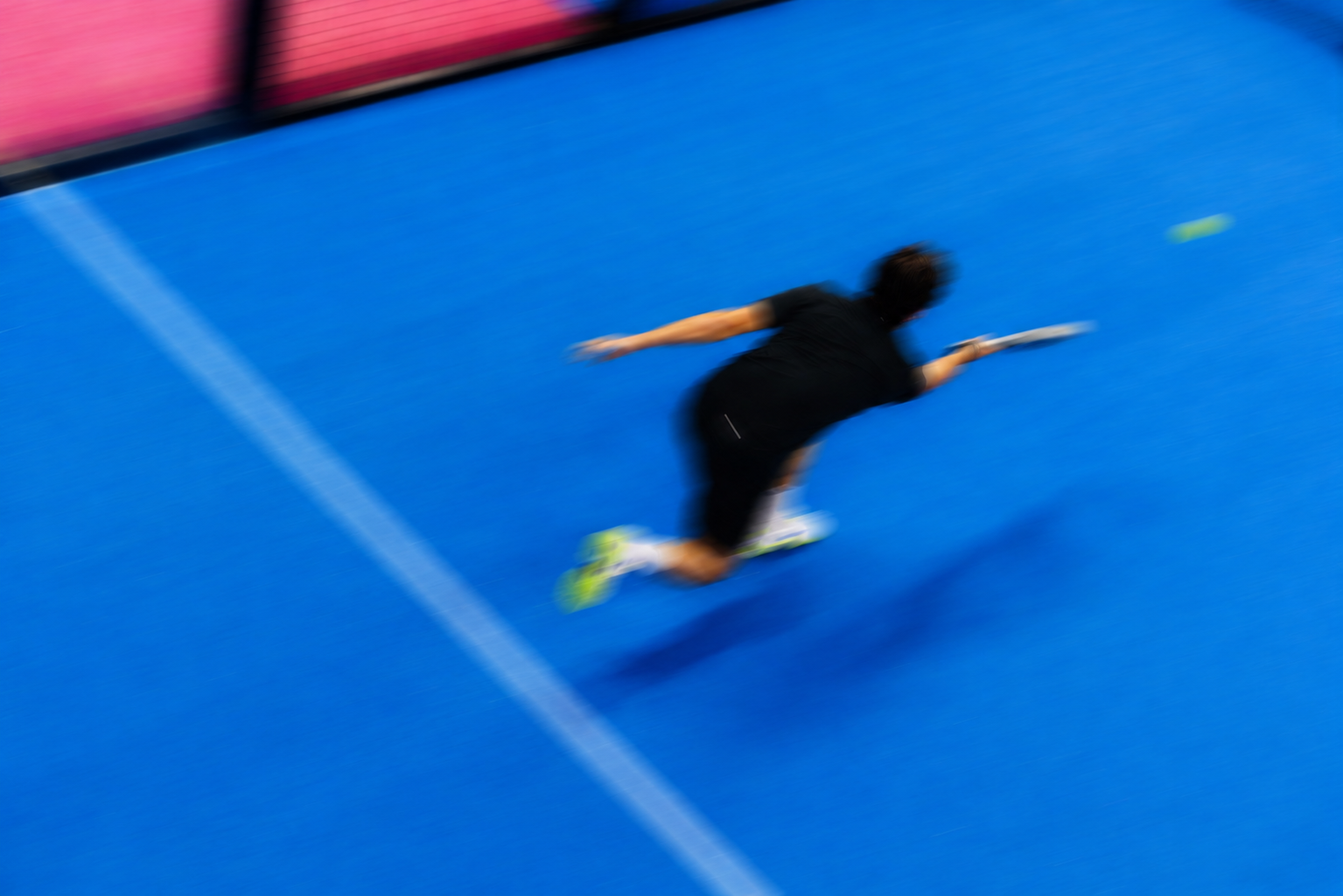 Padel player diving across a blue court, captured in motion blur
